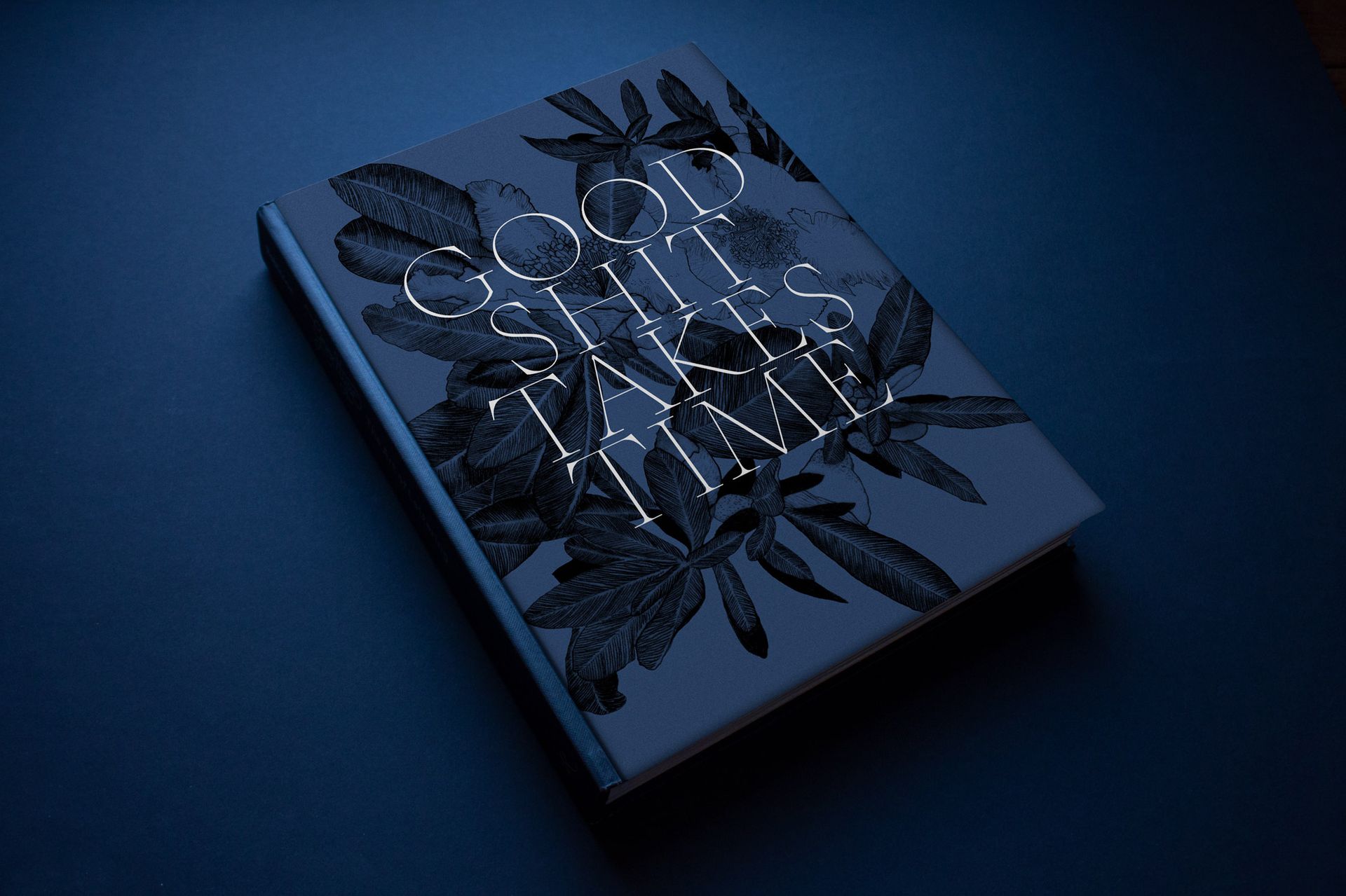 A dark blue book with silver, dotted typography and botanical illustrations on the cover, set against a dark background.
