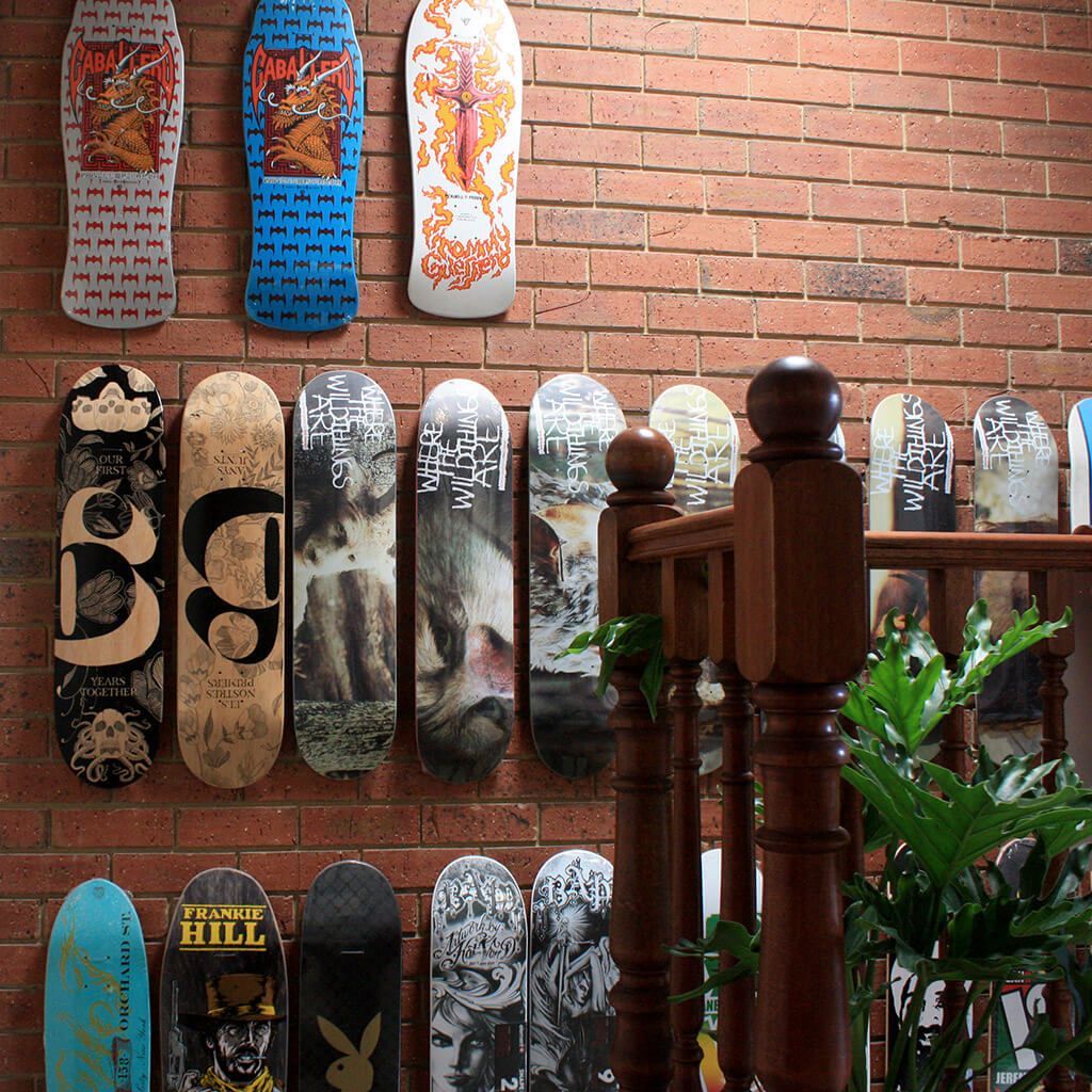 A collection of colorful graphic skateboards mounted on a textured brick wall behind a wooden staircase railing.
