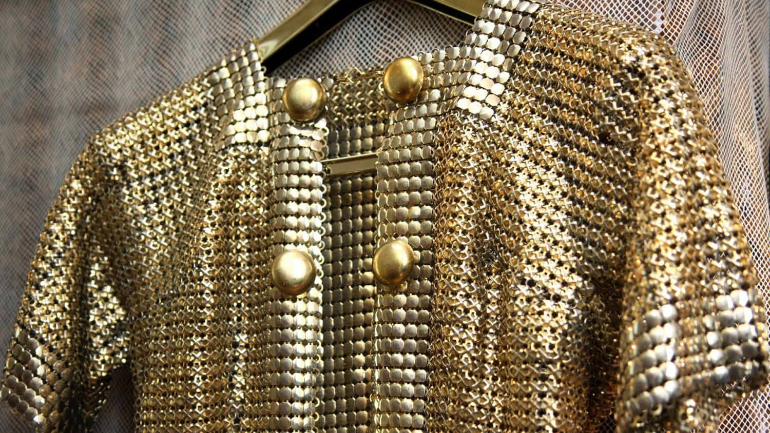 Gold sequined jacket on a hanger, with large decorative gold buttons and textured metallic fabric.