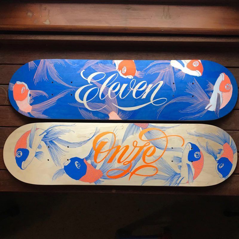 Two skateboards with stylized koi fish designs. The top is blue with white text