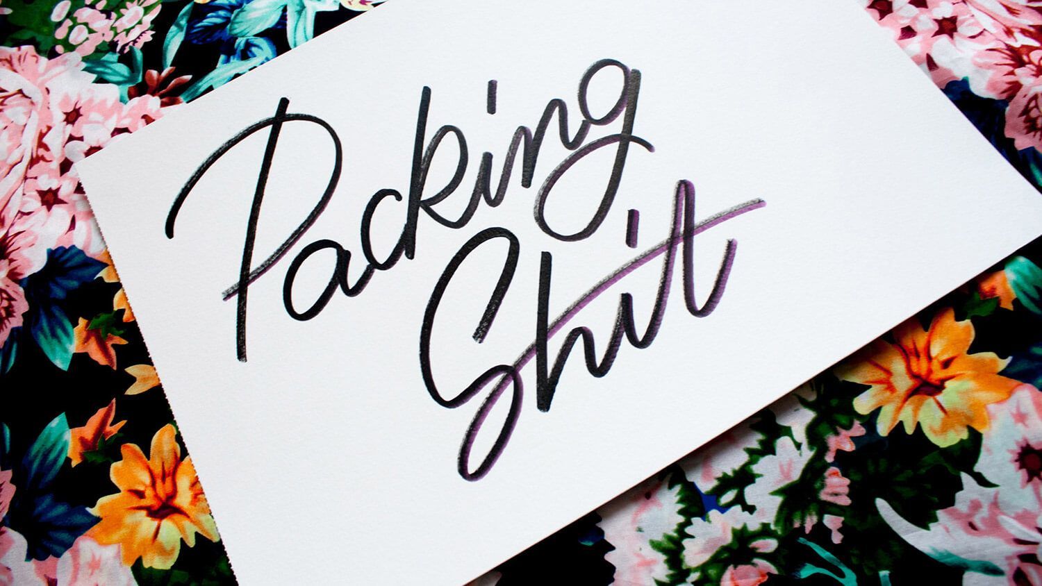 “Packing Shit” handwritten on a white card over a colorful floral background