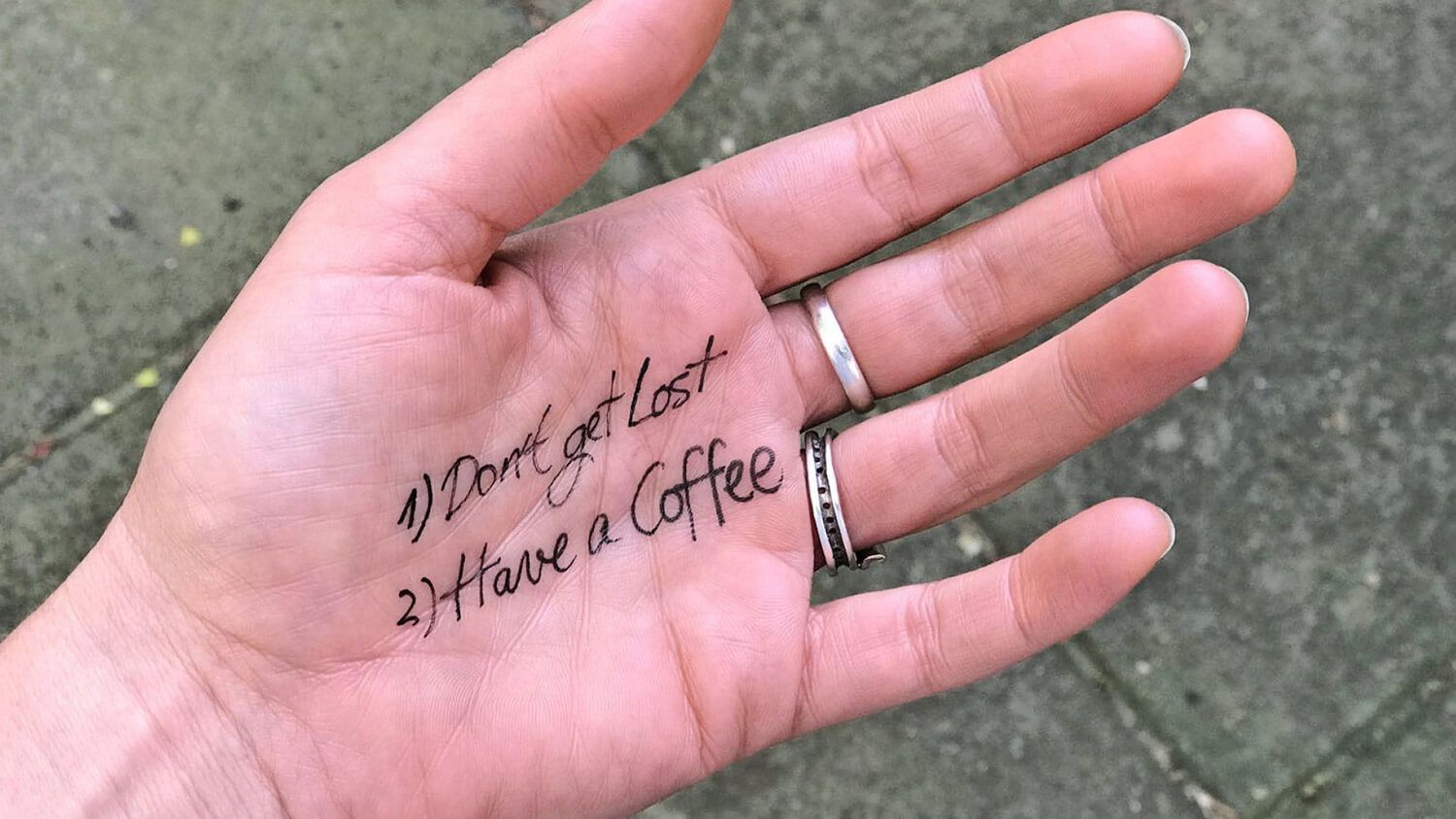 Palm with handwritten note: “Don’t get lost” and “Have a coffee,” wearing silver rings.