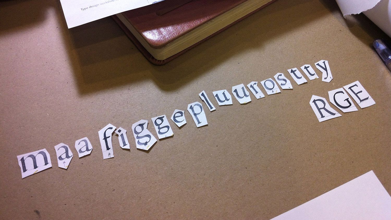 Cutout letters spelling “maizeglutnous RGE” on a brown tabletop next to papers and a notebook