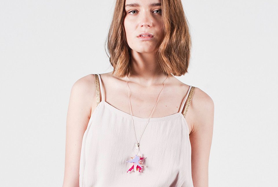 Young woman in a white top with a pink necklace, standing against a plain white background