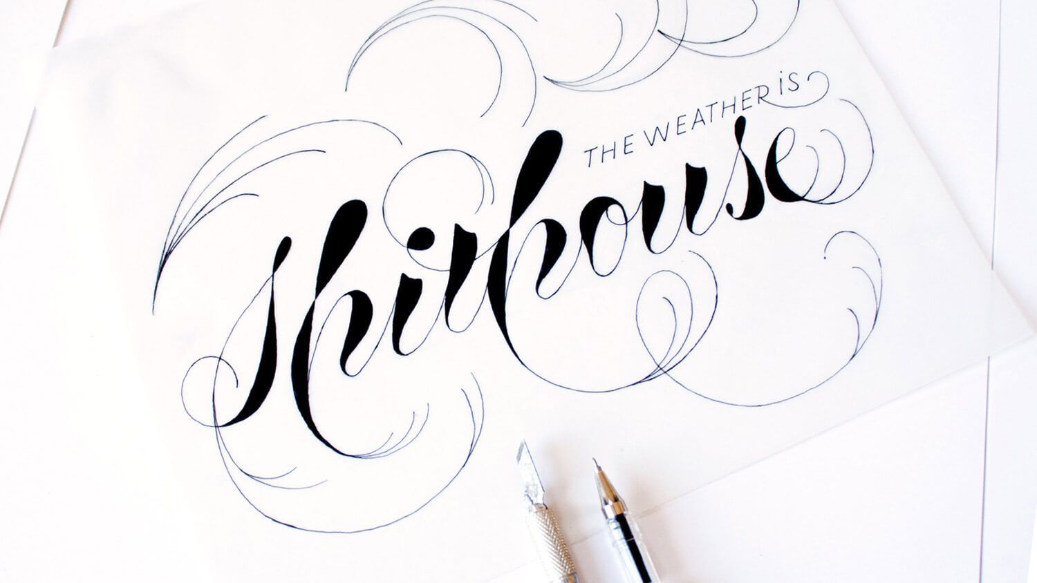 Hand lettering sketch of “Whirhouse” on white paper with a pen nearby