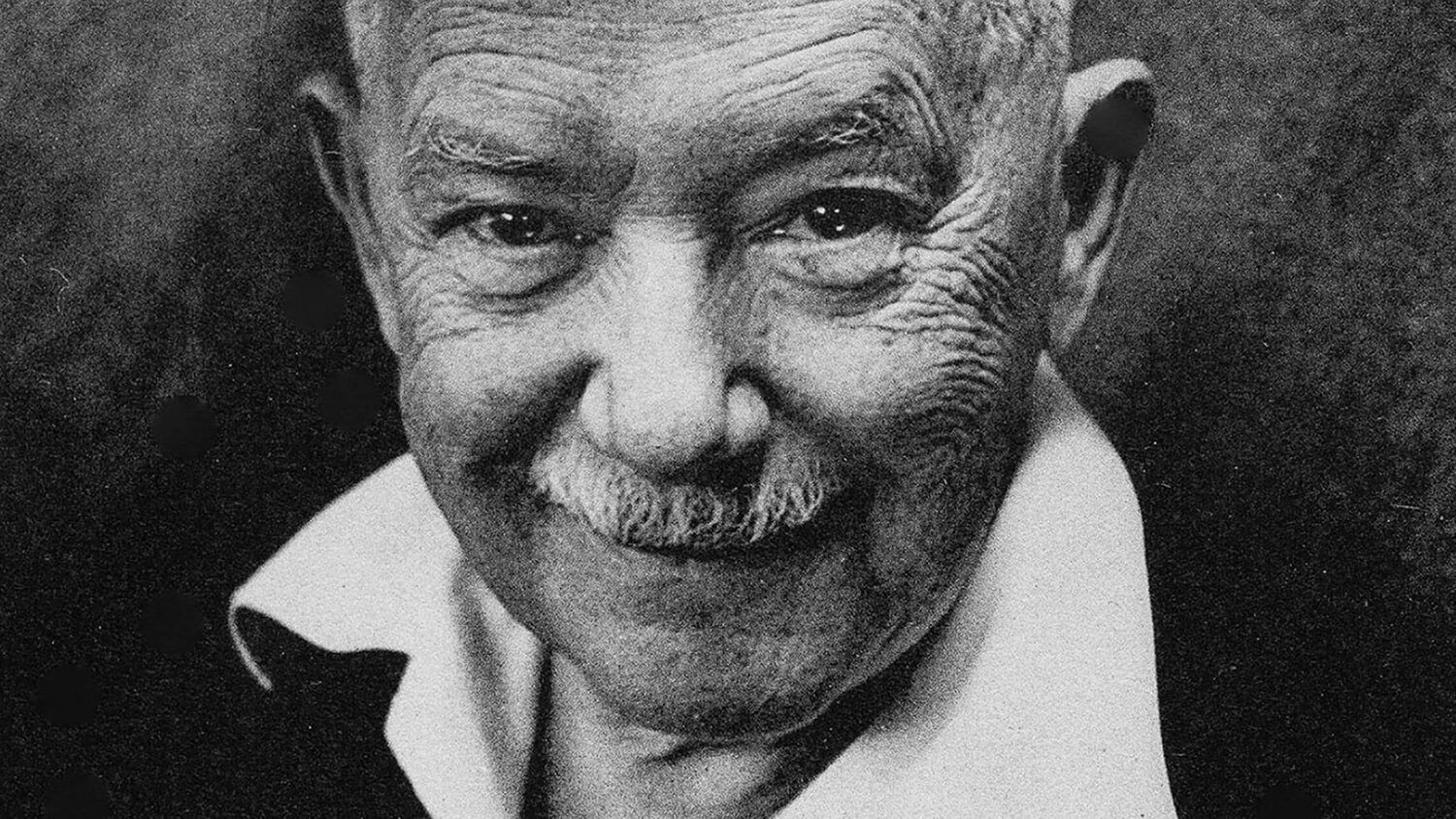 Black-and-white close-up portrait of an elderly man with a slight smile, wearing a collared shirt and jacket.