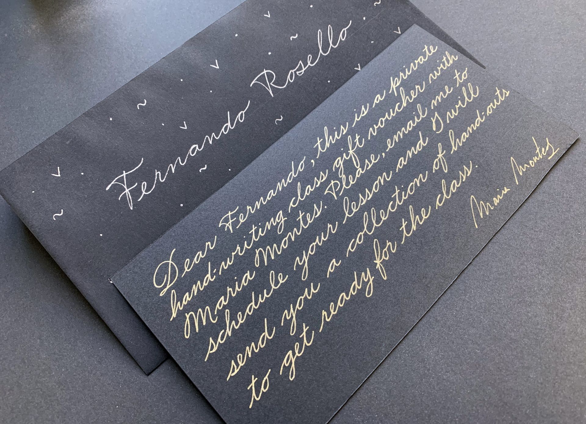 A black envelope and handwritten note in metallic ink, addressed to Fernando Rosello regarding a calligraphy class voucher.