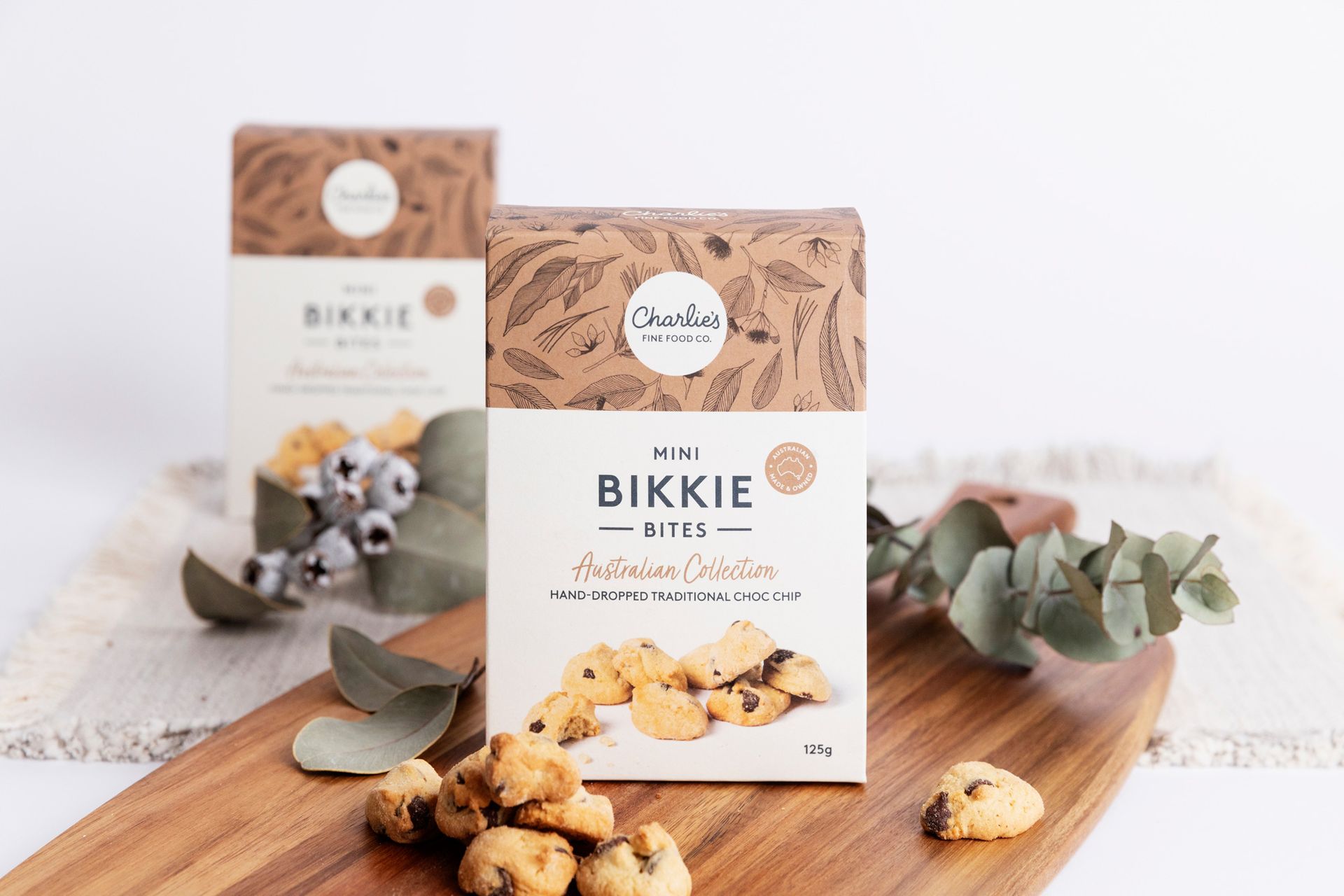 Bikkie cookie boxes on a wooden board with eucalyptus leaves and cookies in a bright studio setting