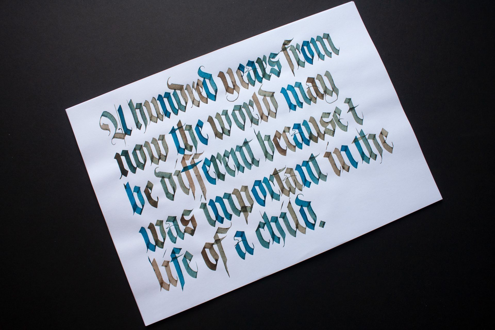 Stylized blue gothic lettering on a tilted white paper against a dark background