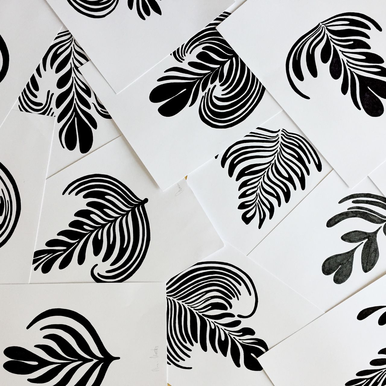 A flat lay of multiple white cards featuring black ink block prints of various fern and leaf botanical patterns.