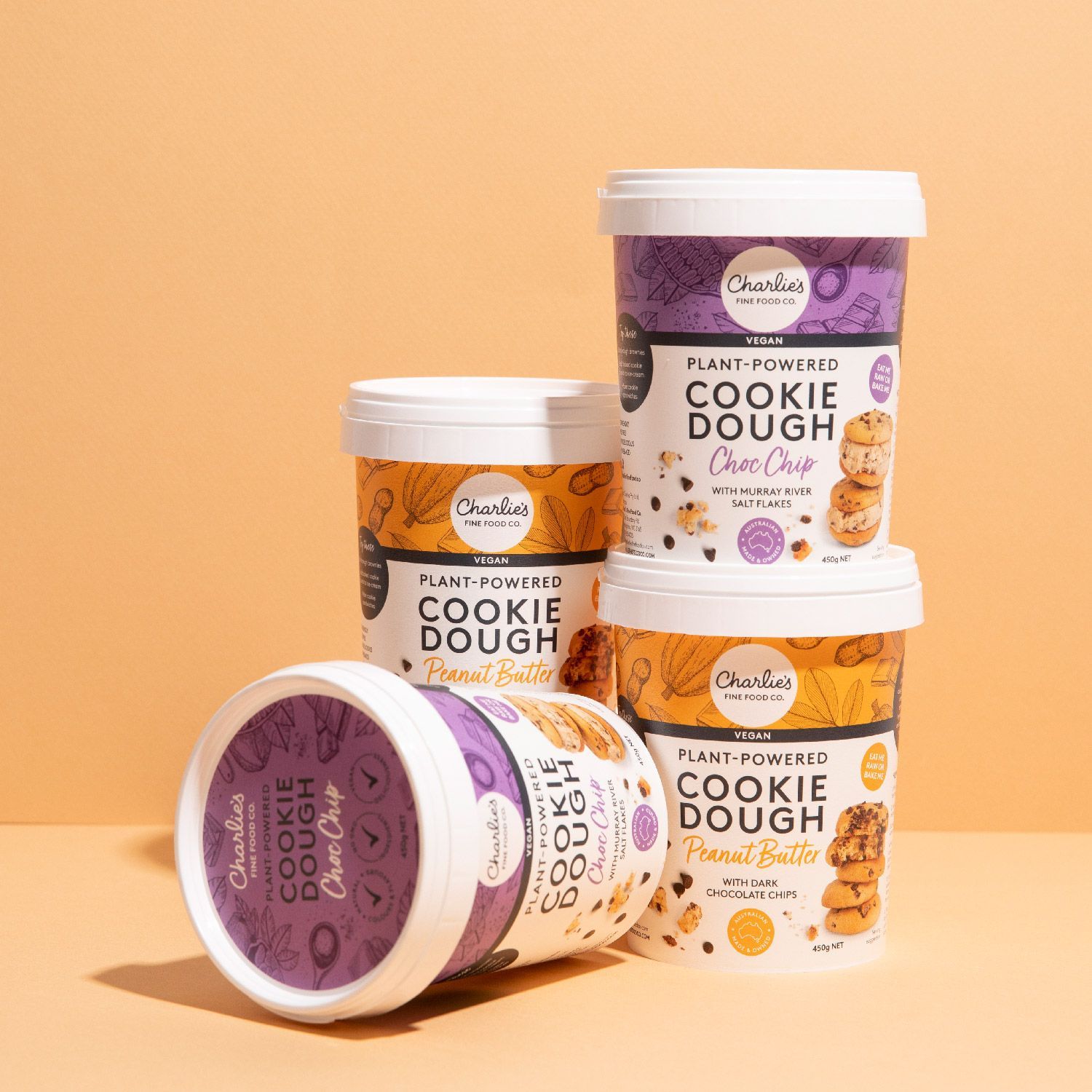 Four stacked cookie dough containers in orange and purple packaging on a peach background