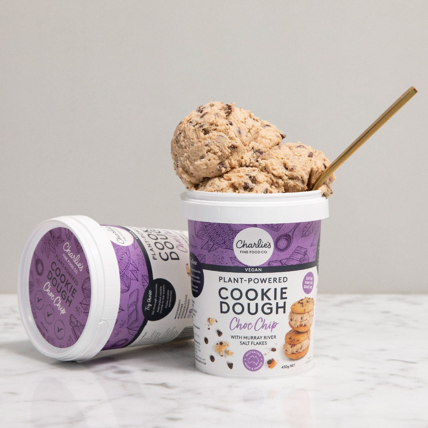 Purple-and-white cookie dough pints, one open with a spoon, on a marble surface