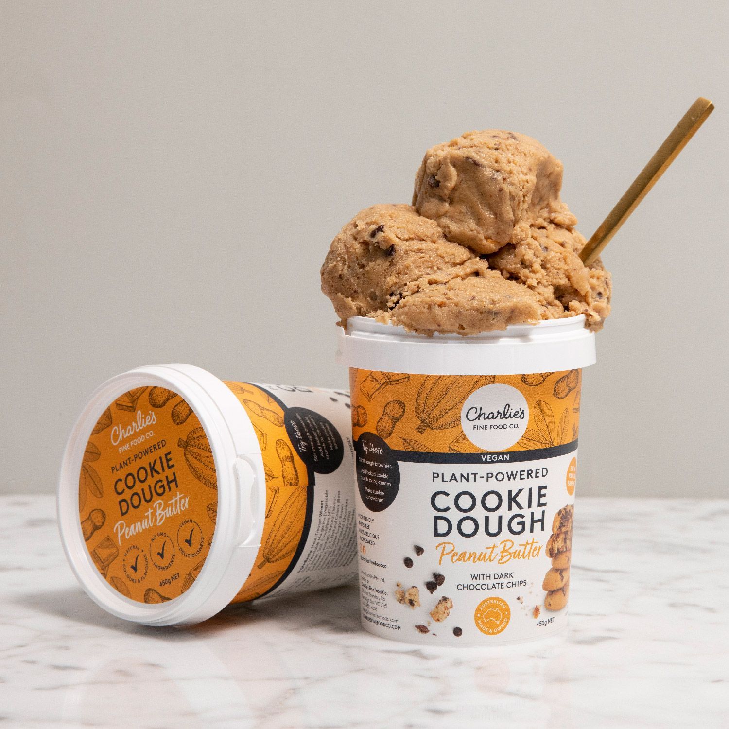 Two tubs of cookie dough ice cream, one open with a scoop and spoon, on a light surface.