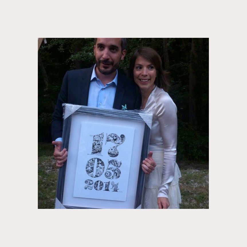 Couple holding framed “Do It” print outdoors, smiling in front of greenery.