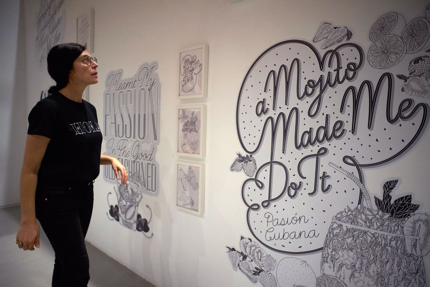 Person in black stands beside a wall mural reading “Mojito Made Me Do It.”