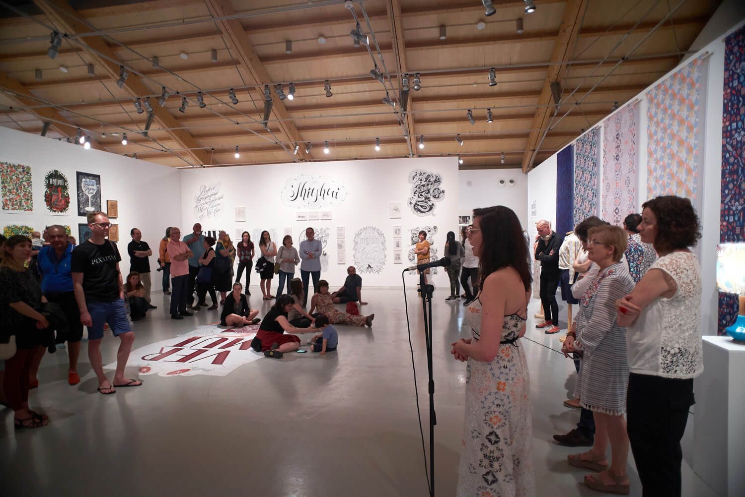 People gathered in a gallery around a floor installation, with artwork displayed on the walls.