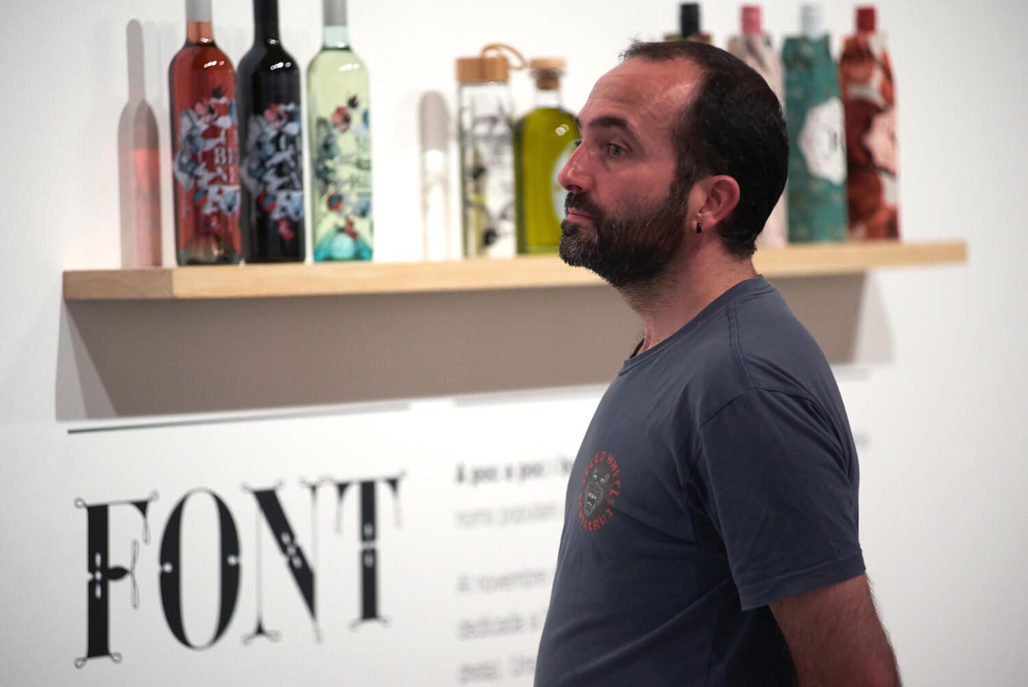 Man standing in profile in front of a shelf with colorful bottles and a large “FONI” sign