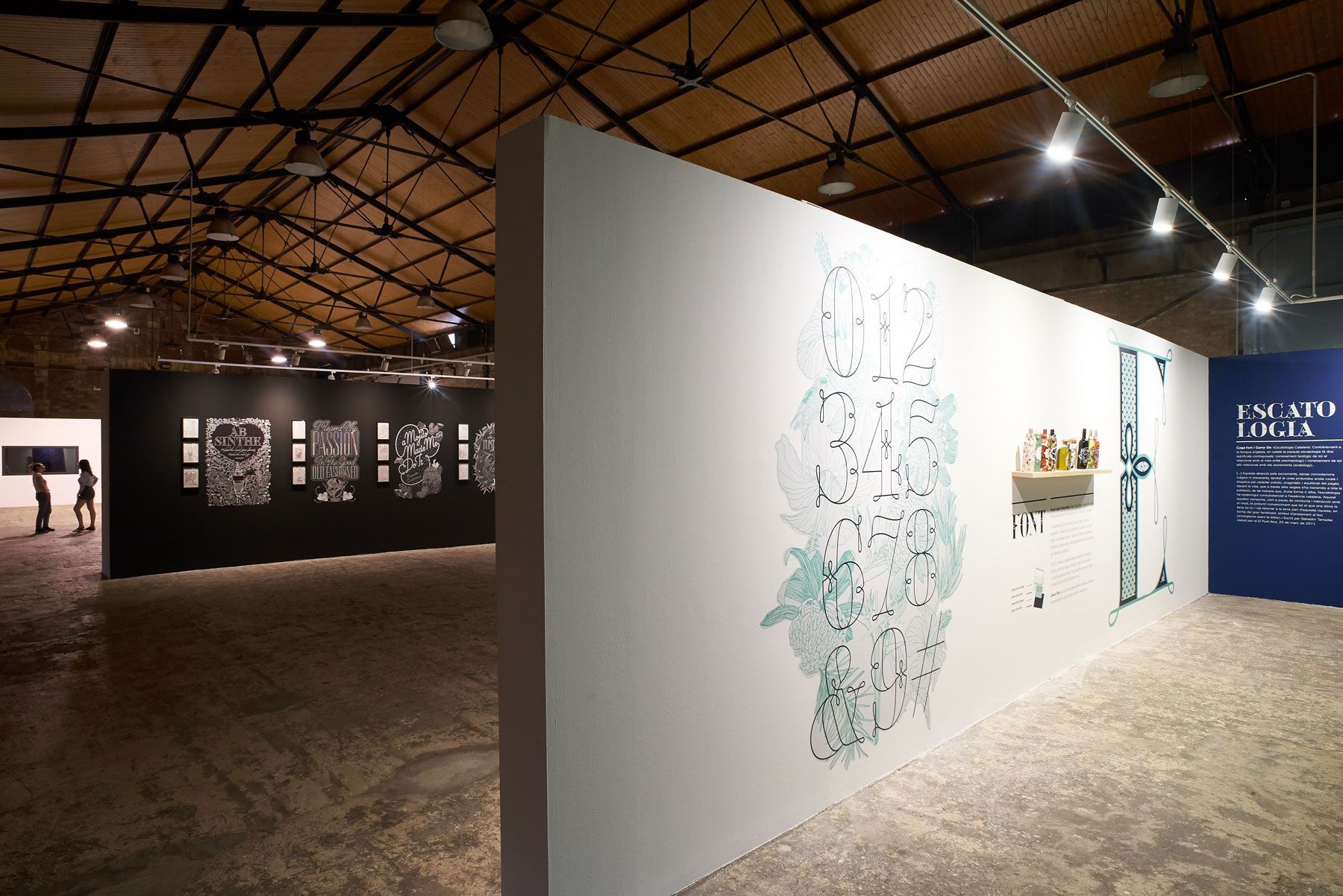 Art gallery interior with white and black exhibit walls, hanging ceiling lights, and a large illustrated panel.