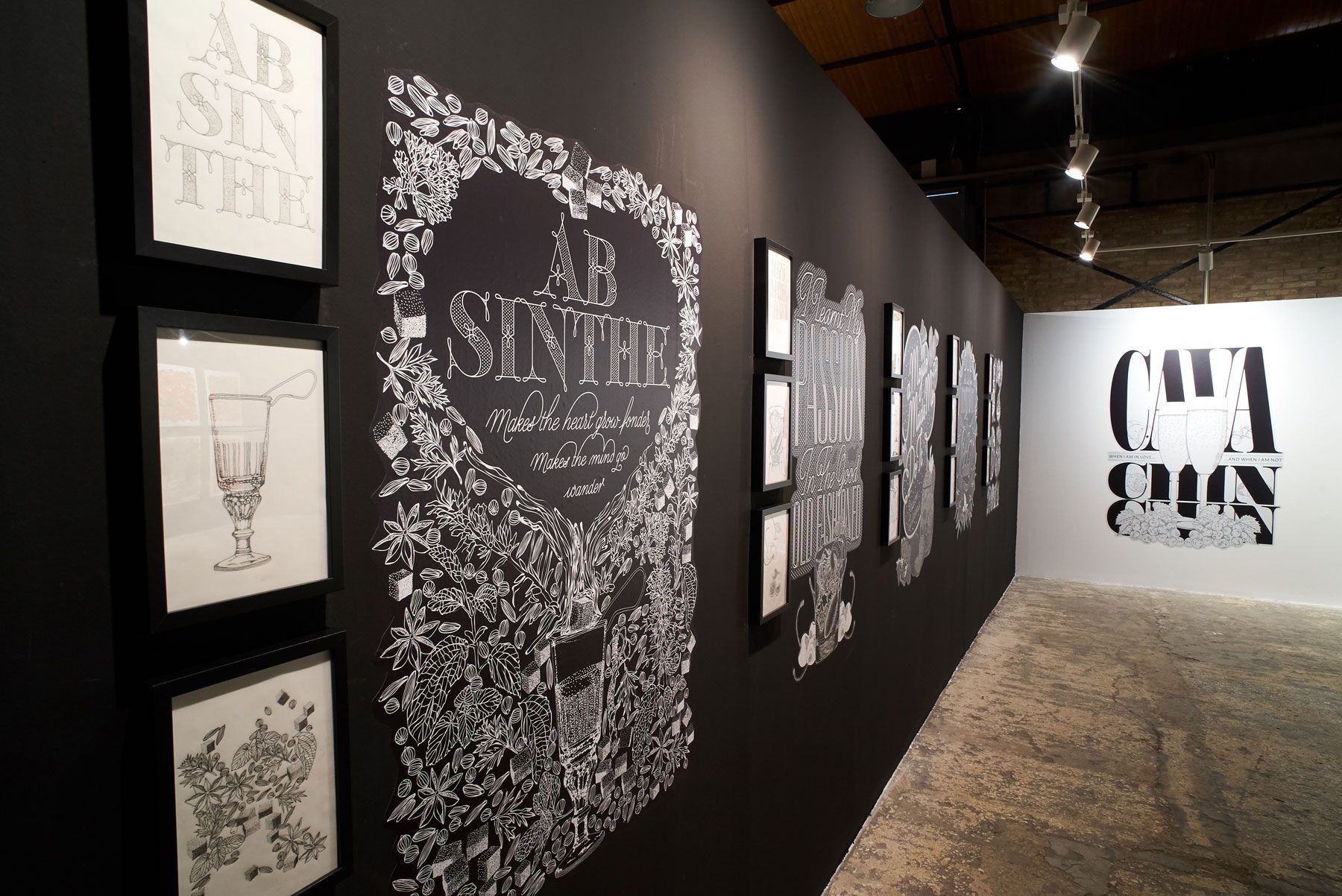 Art gallery hallway with black walls, framed typography prints, and a large mural at the end.