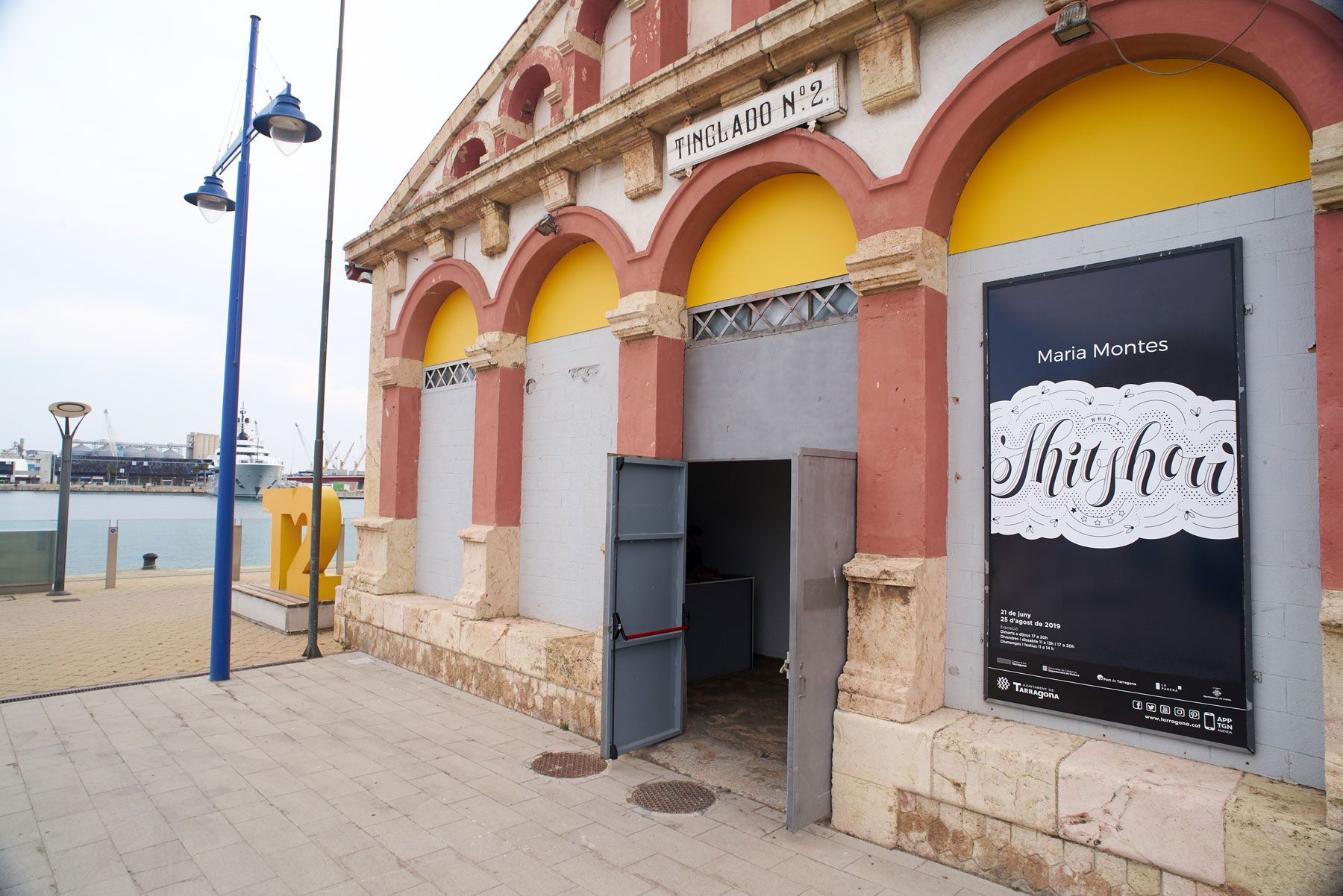 Yellow-arched building facade by the waterfront with an open doorway and postered windows
