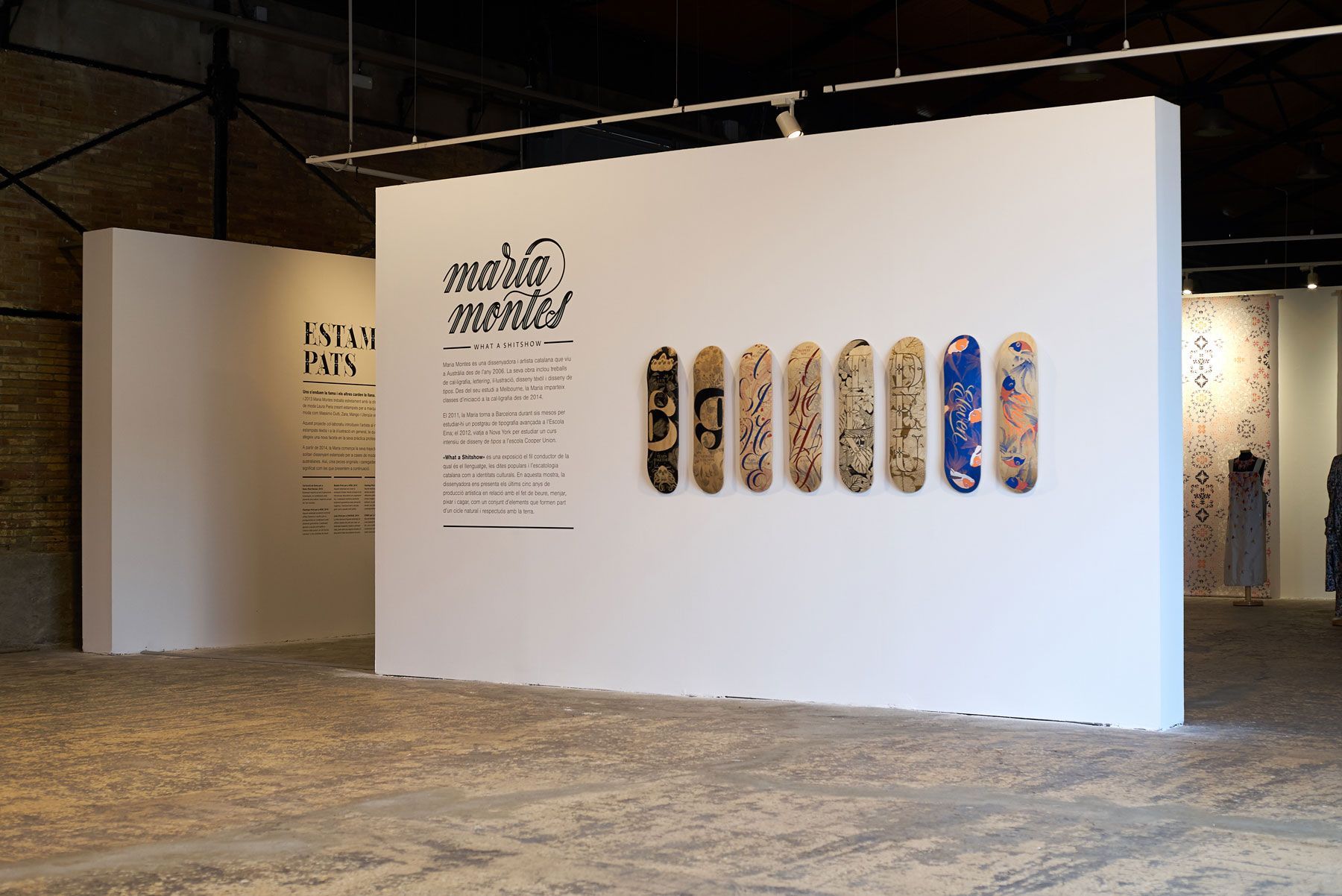 An exhibition display featuring a wall of text and eight decorative skateboards mounted in a row inside a gallery space.