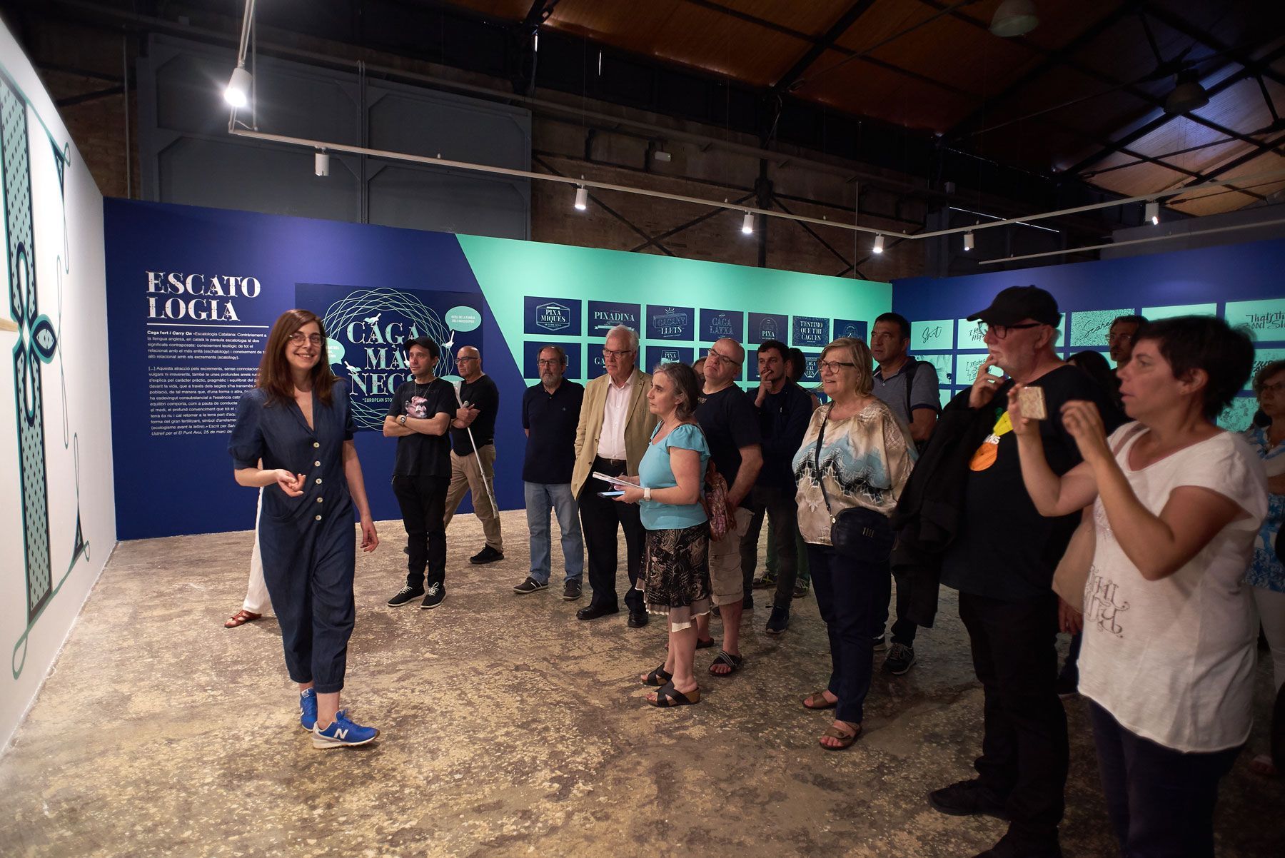 Gallery tour with a speaker addressing a small group in a blue-walled exhibition space.