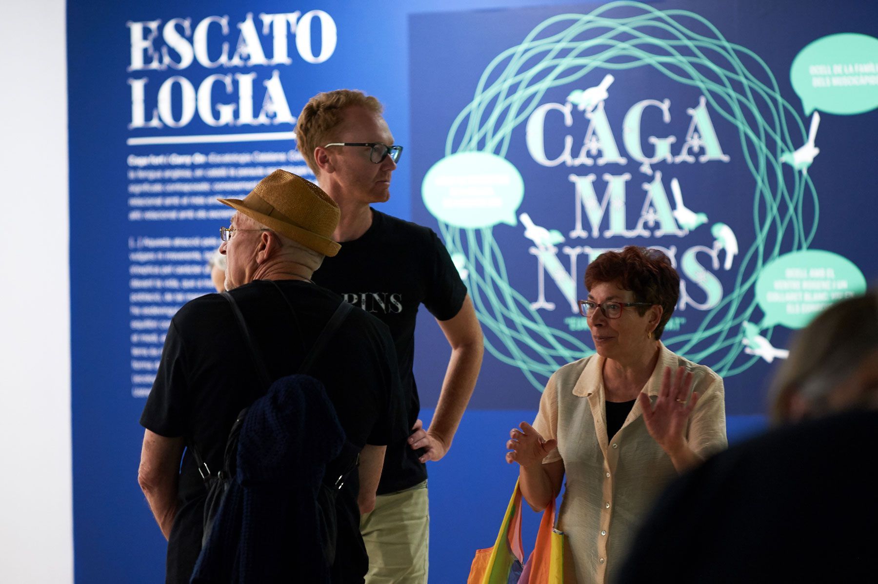 People standing in front of blue exhibition posters with large white text and a circular graphic.