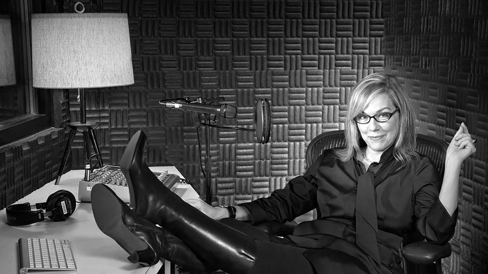 Person reclining in an armchair in a studio, with a desk, lamp, and soundproof wall panels behind them.