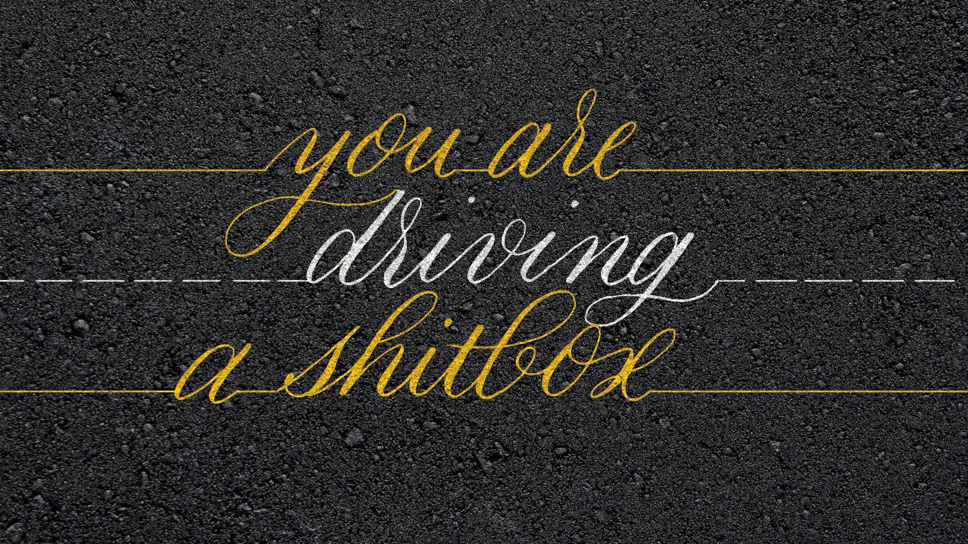 Handwritten yellow text on dark pavement reads, “you are driving a shitbox.”