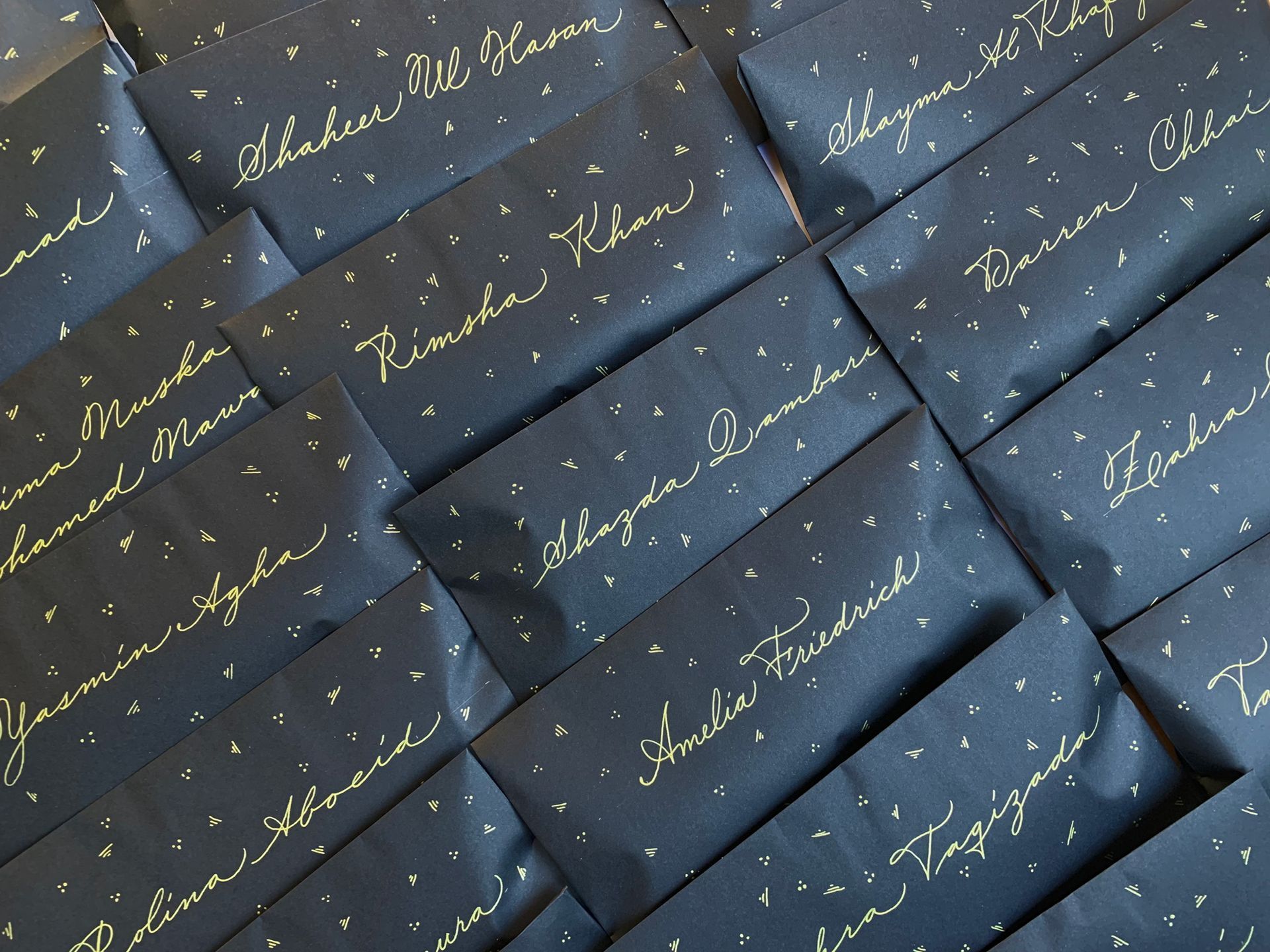 Dark envelopes with speckled white patterns, each featuring unique white handwritten names in elegant cursive script.