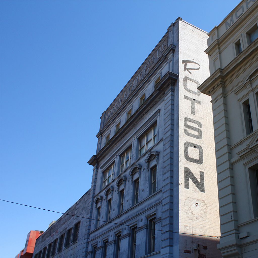 Corner of a city building with a vertical “ROTTSON” sign against a blue sky