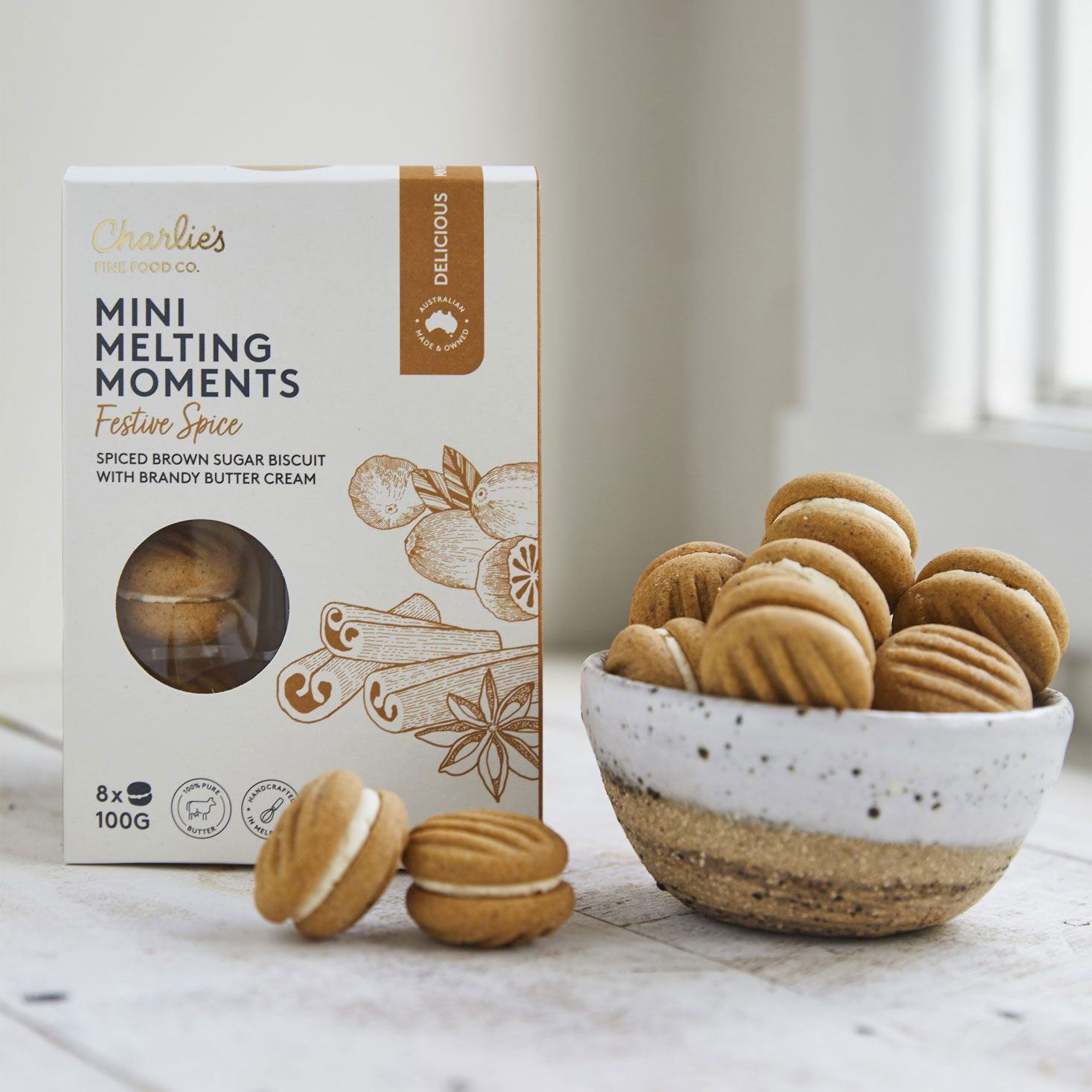 Box of mini melting moments cookies beside a bowl of sandwich cookies on a marble surface