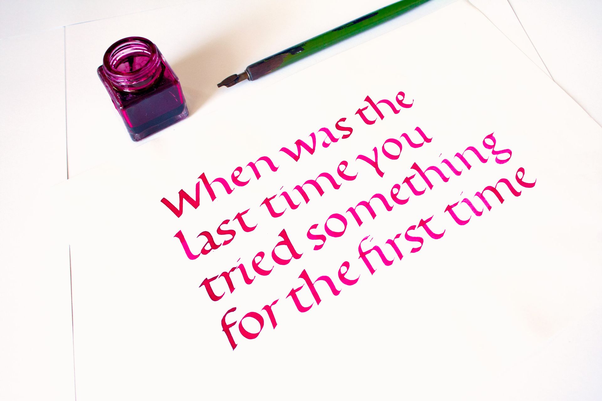 Pink ink quote on white paper beside a purple ink stamp and green pen.