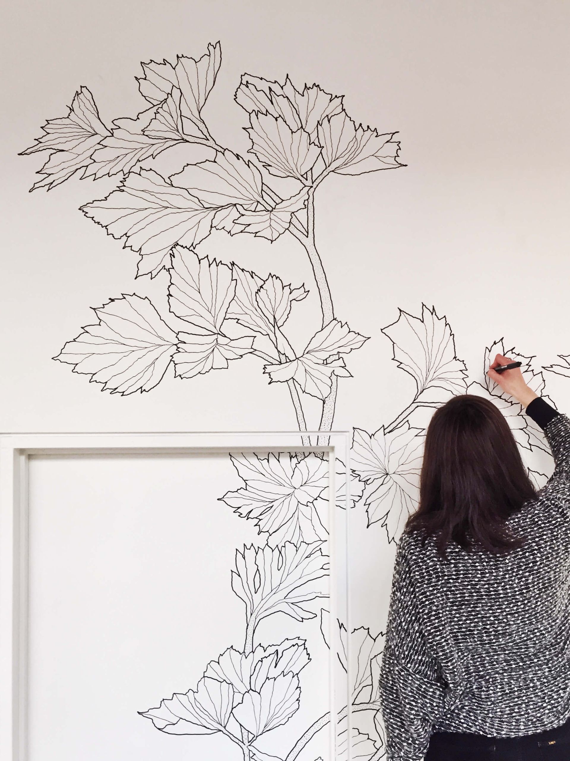 Person applying a leafy black wall mural in a bright room