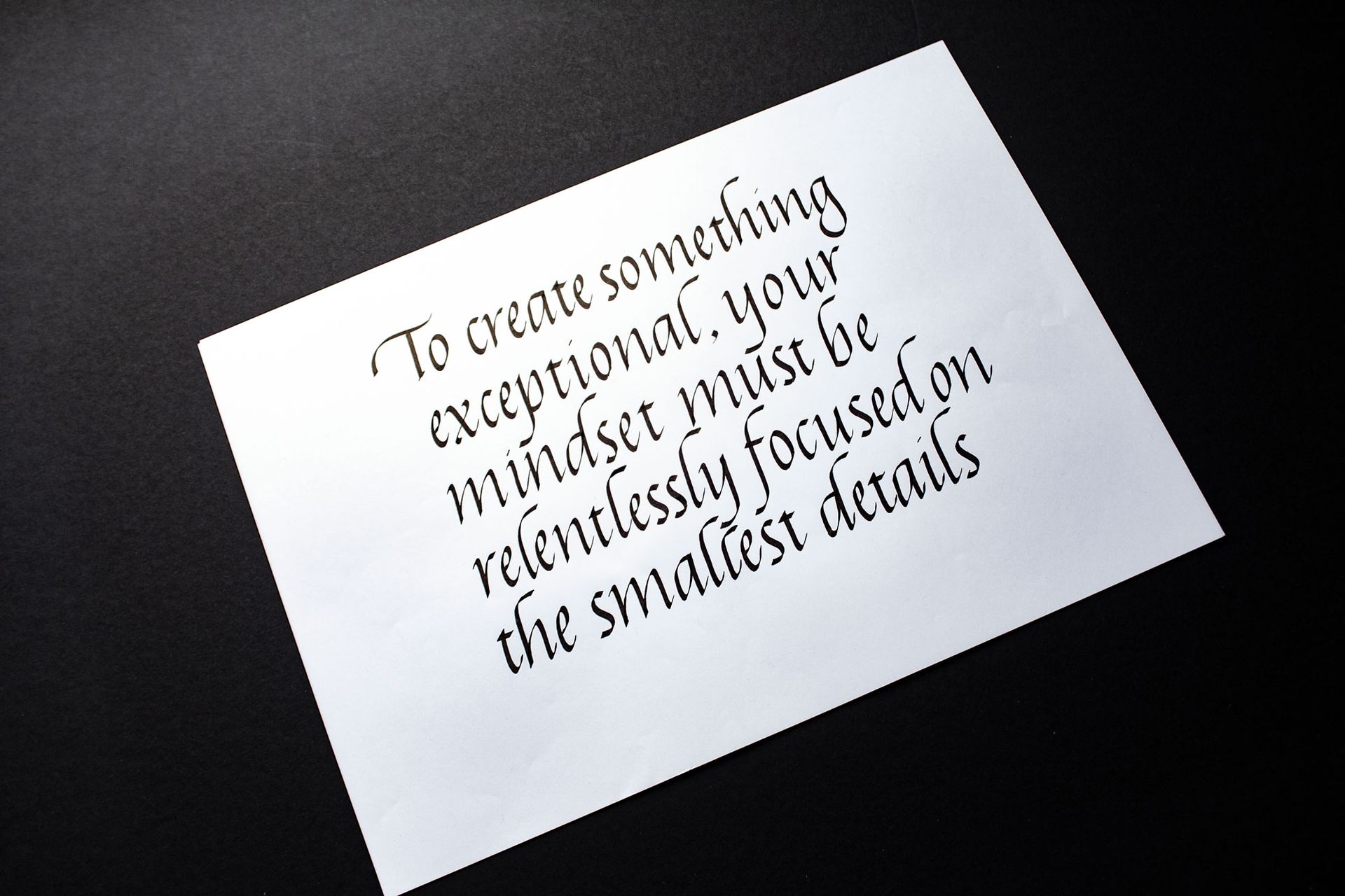 Tilted white card with a motivational quote in black cursive text on a light gray background
