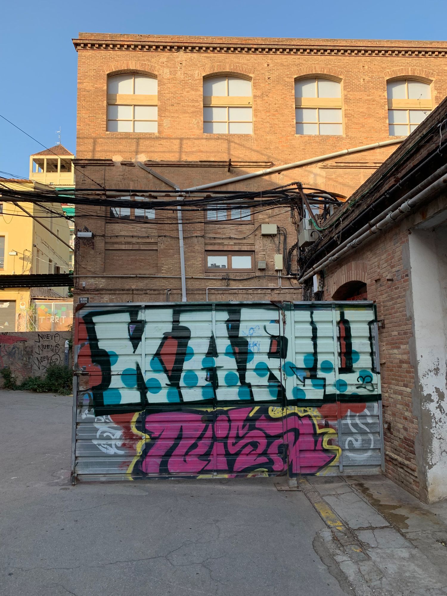 Graffiti-covered brick wall in an alley with a brick building and blue sky behind it