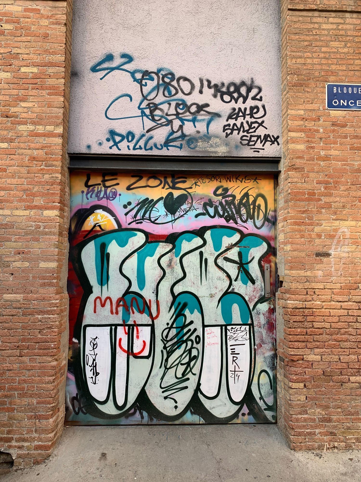 Graffiti-covered metal door in a brick alley, with colorful tags and murals on surrounding walls