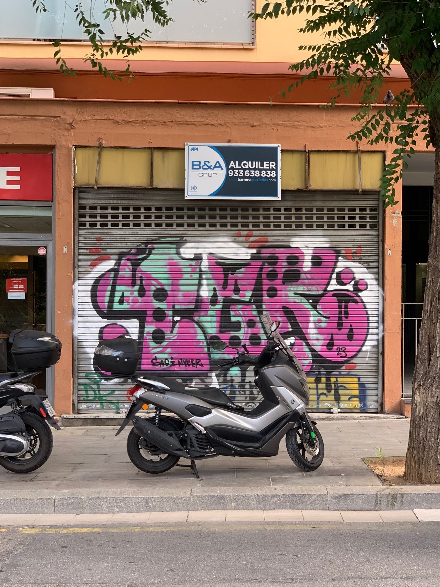 Closed storefront with pink graffiti, a parked scooter, and a blue sign above a metal shutter.