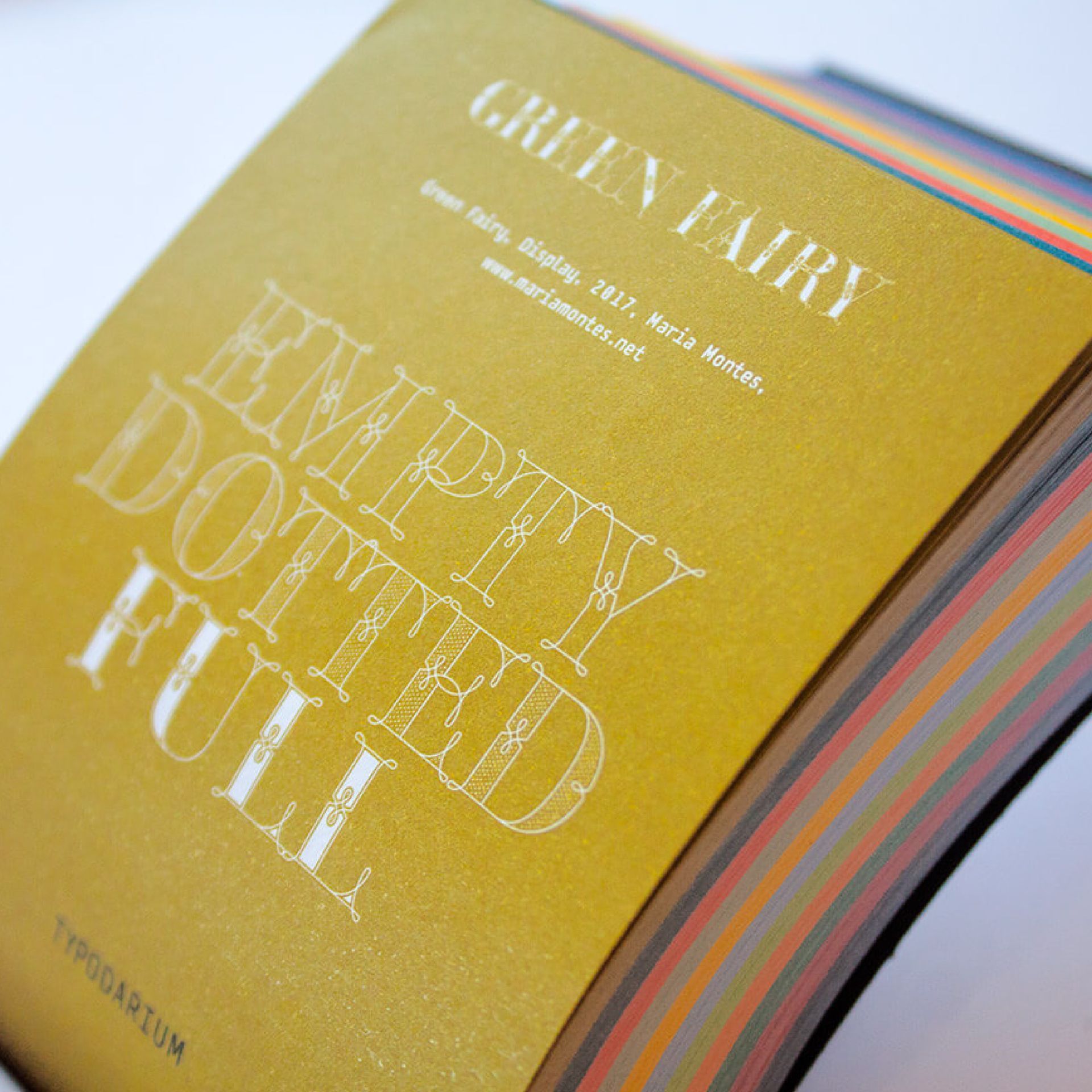 Green Fairy Font. Close-up of a gold book cover with embossed white text and multicolored page edges