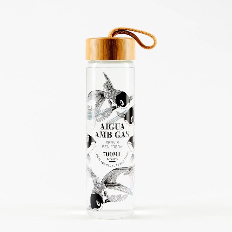 A clear glass water bottle with a wooden cap and handle, featuring black-and-white fish illustrations and Catalan text.
