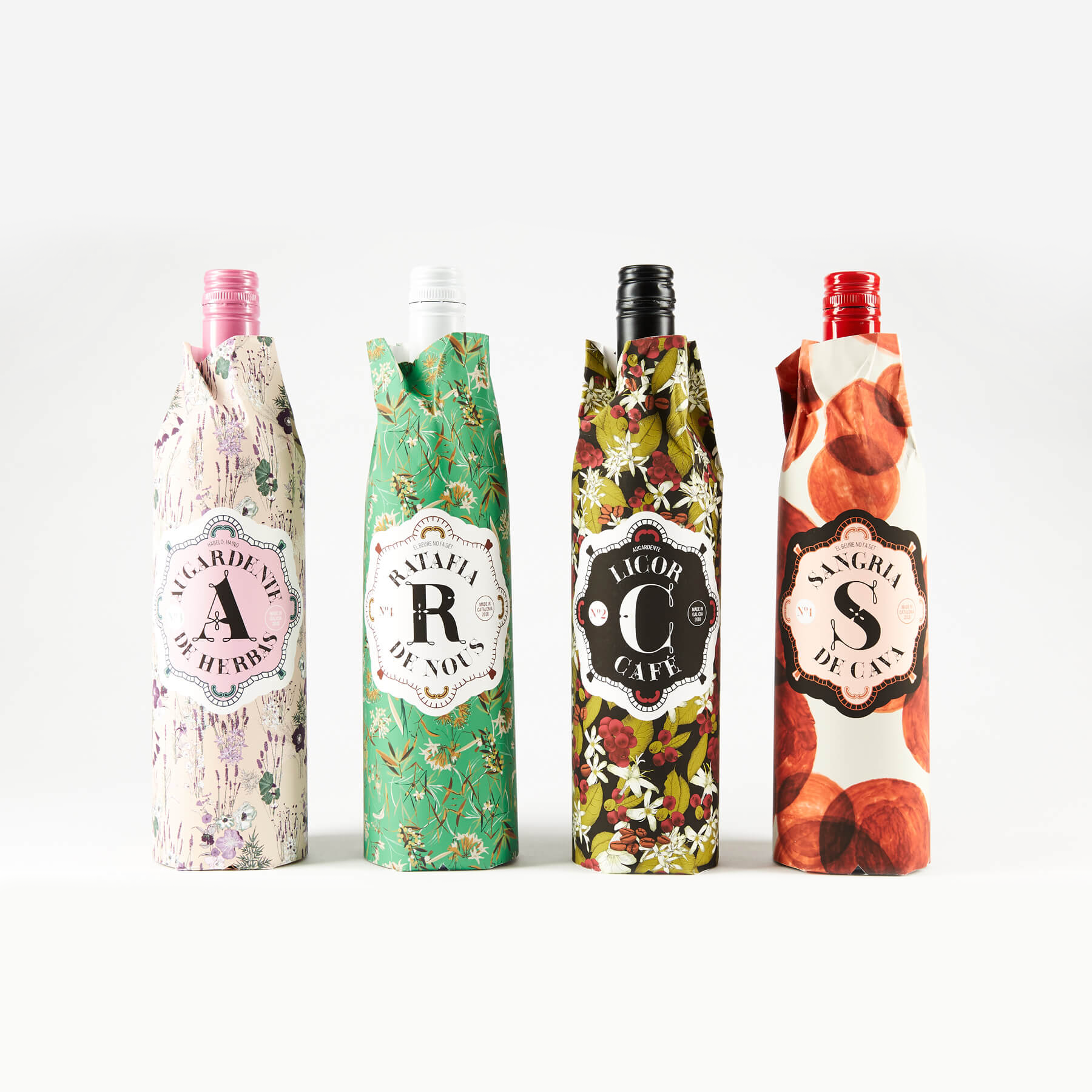 Four wine bottles in patterned paper wrappers, each with a large, distinct letter (A, R, C, S) on the label.