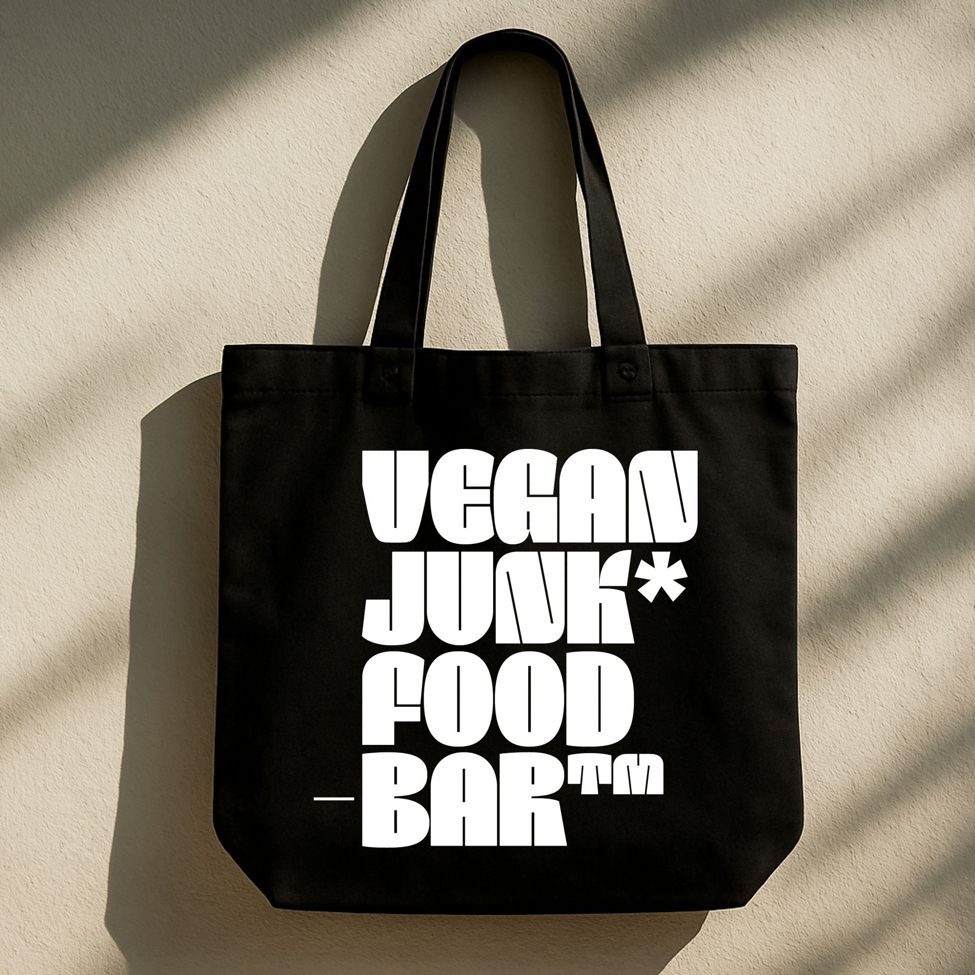 Black tote bag with bold white “VEGAN JUNK FOOD BAR” text on a beige background