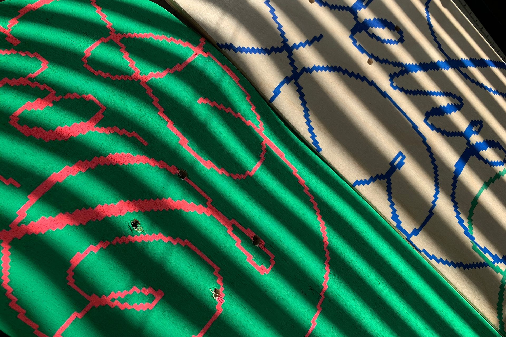 Two skateboards, one green with red swirls and one white with blue, viewed under striped shadows.