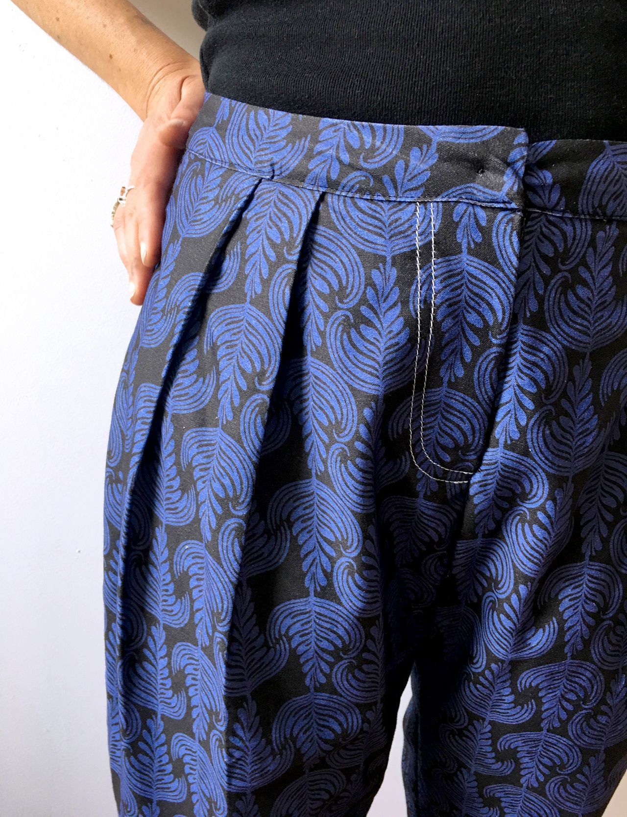 Blue patterned pants with pleats, shown at the waist and hip against a light background
