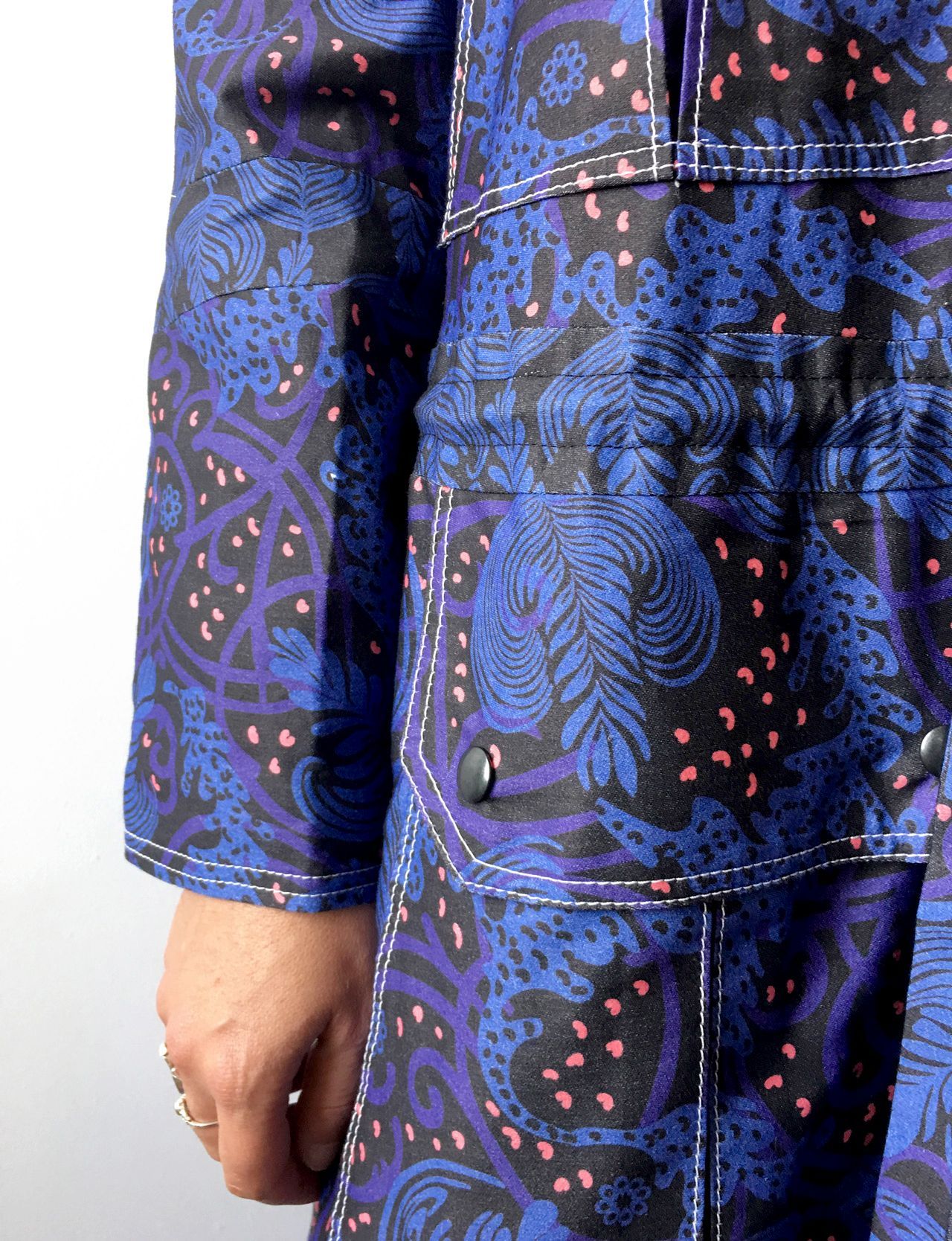 Close-up of a person wearing a blue and black jacket with a swirling botanical pattern and white stitching detail.