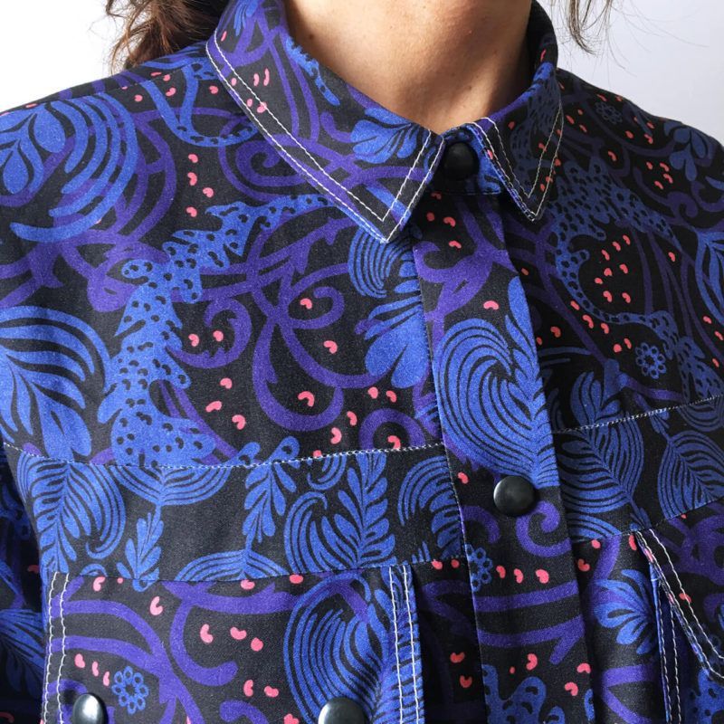 A button-up shirt featuring a vibrant, blue and black floral pattern with small pink accents and visible topstitching.