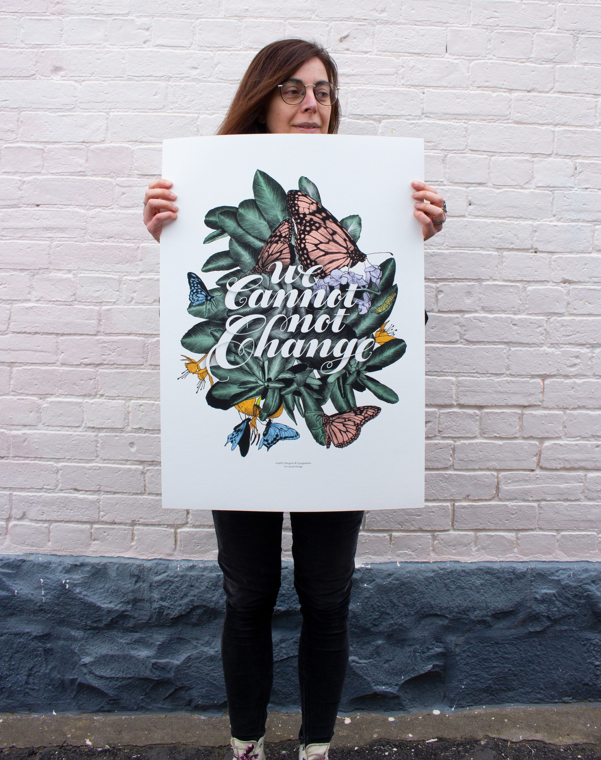 Person holding a white poster with a floral “Farmers Gonna Farmer” design against a brick wall