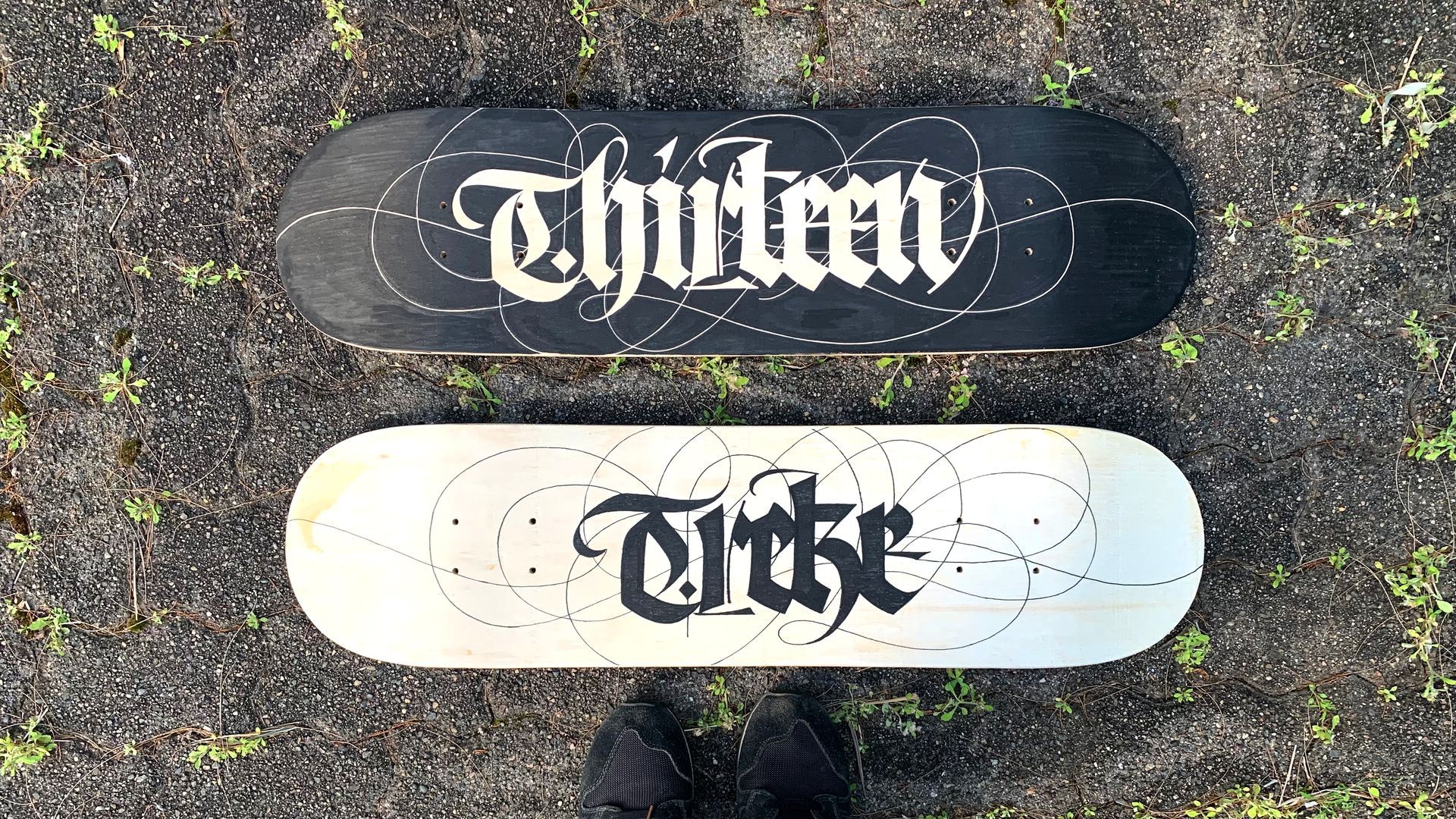 Two skateboard decks lying on ground: one black with white text