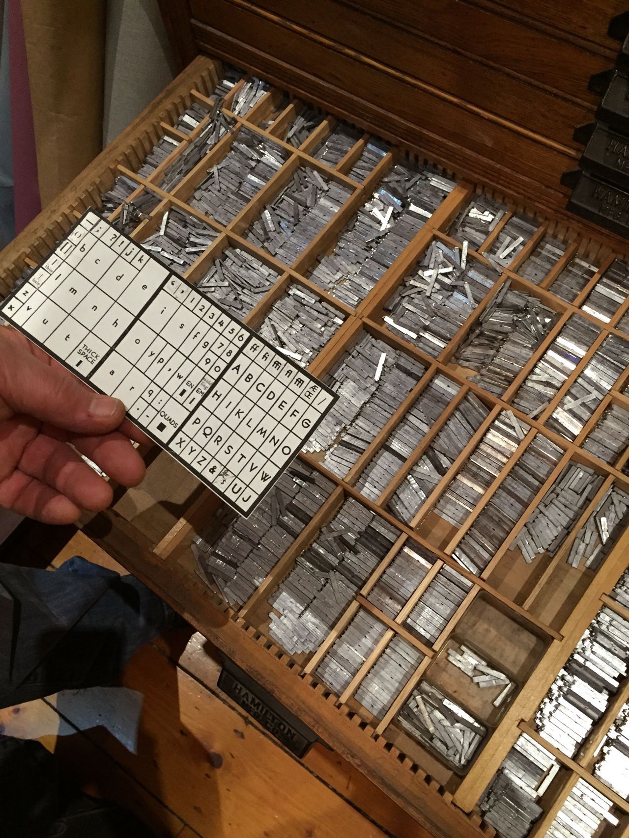 Hand holding a letterpress type tray with metal type blocks in a wooden case