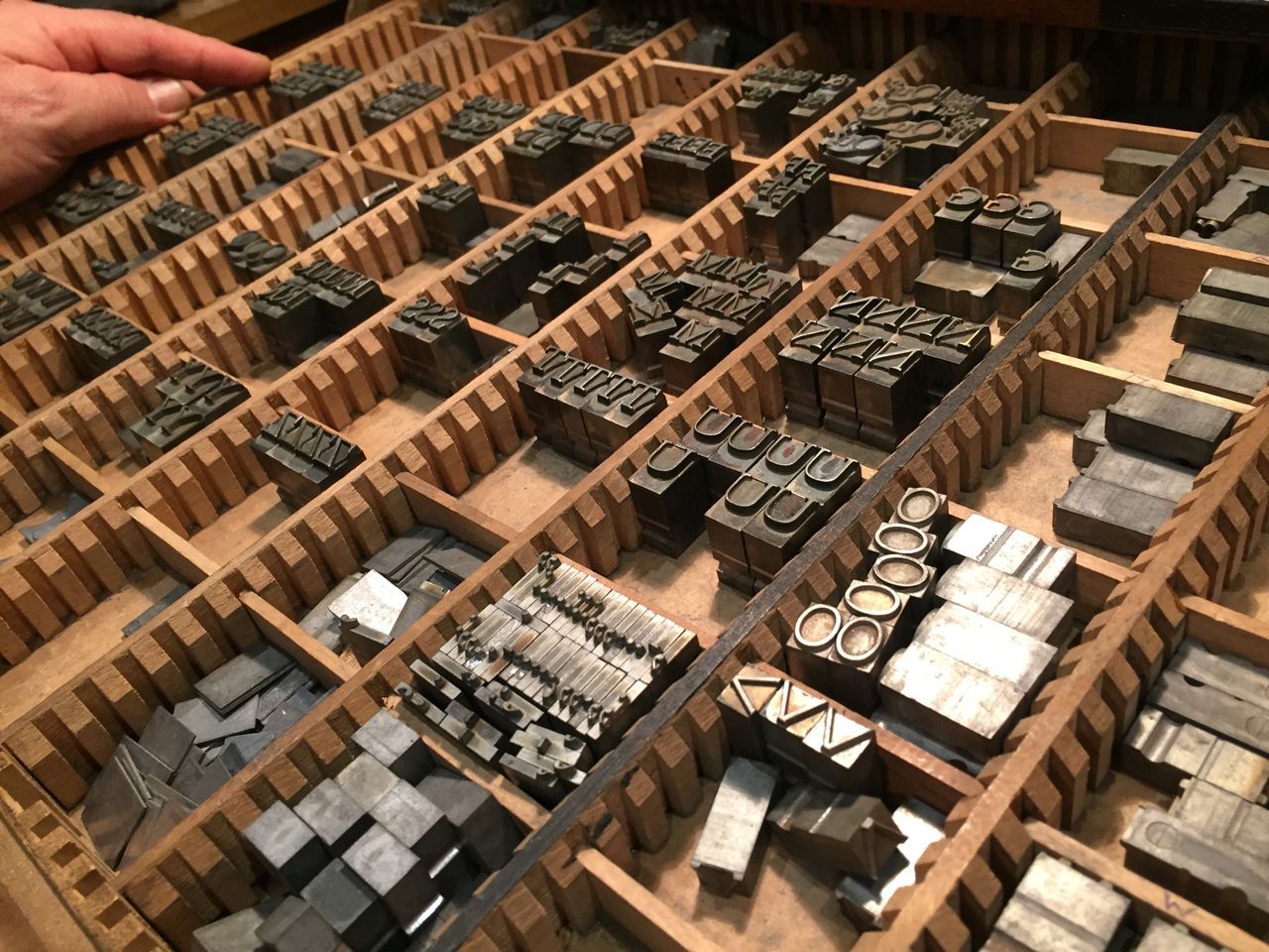 Hand sorting drawers of vintage metal type blocks in a print shop cabinet